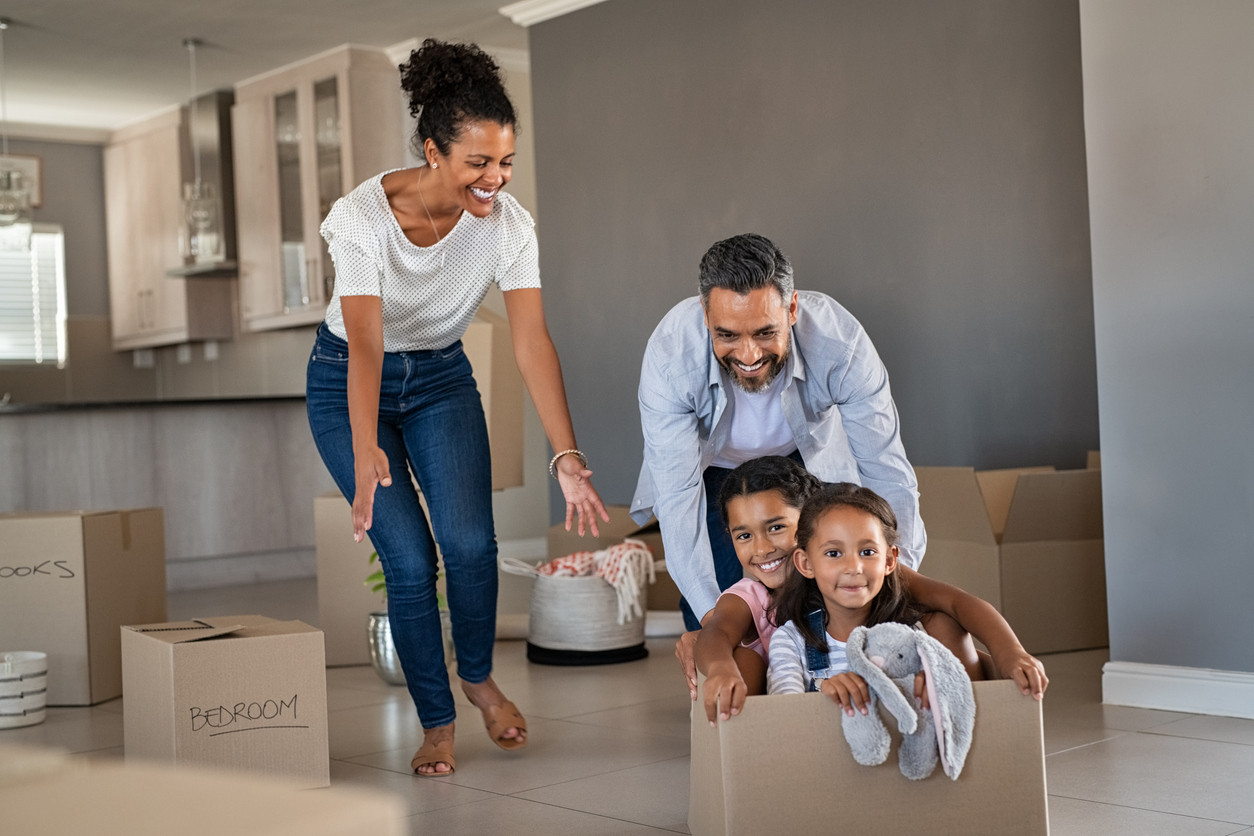 Happy indian father playing with daughters sitting in carton box at new home. Happy multiethnic family having fun together in new house. Smiling dad pushing excited little girls in cardboard box after relocation.
